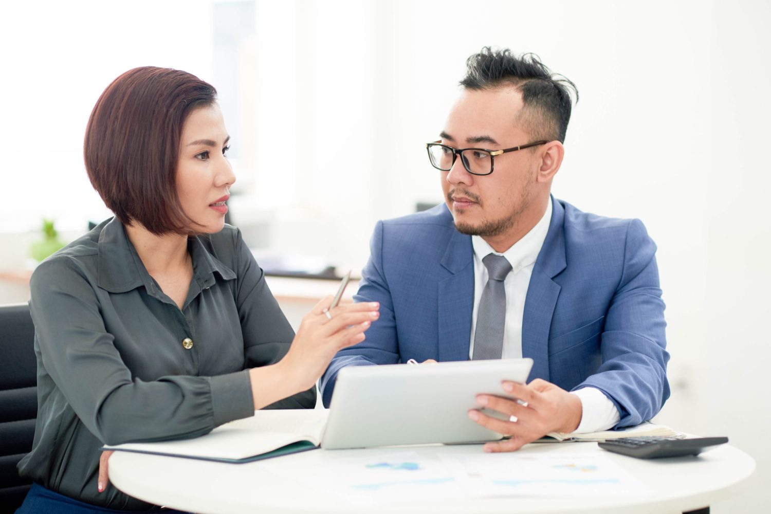 asian-man-woman-business-attire-sitting-indoors-with-tablet-talking